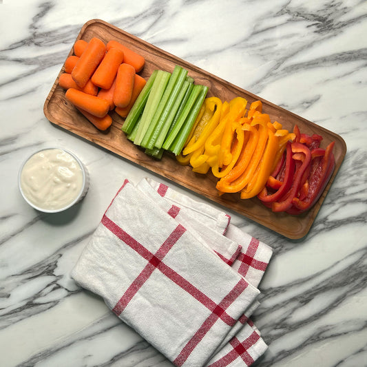 Platter of sliced carrots, celery, and bell peppers with a small bowl of dip on a marble surface.