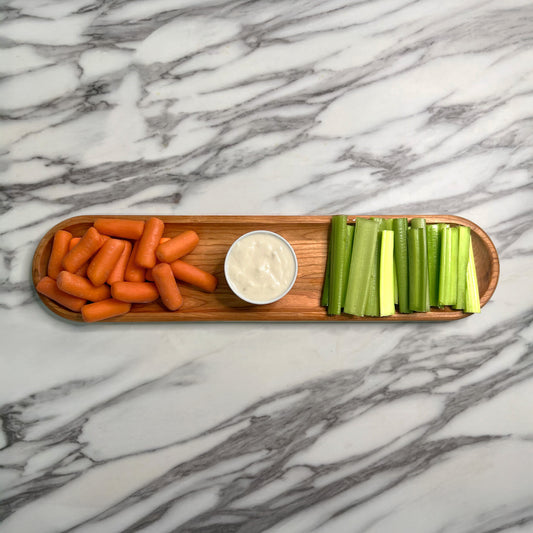 Wooden platter with carrots, celery, and a small bowl of dip on a marble surface