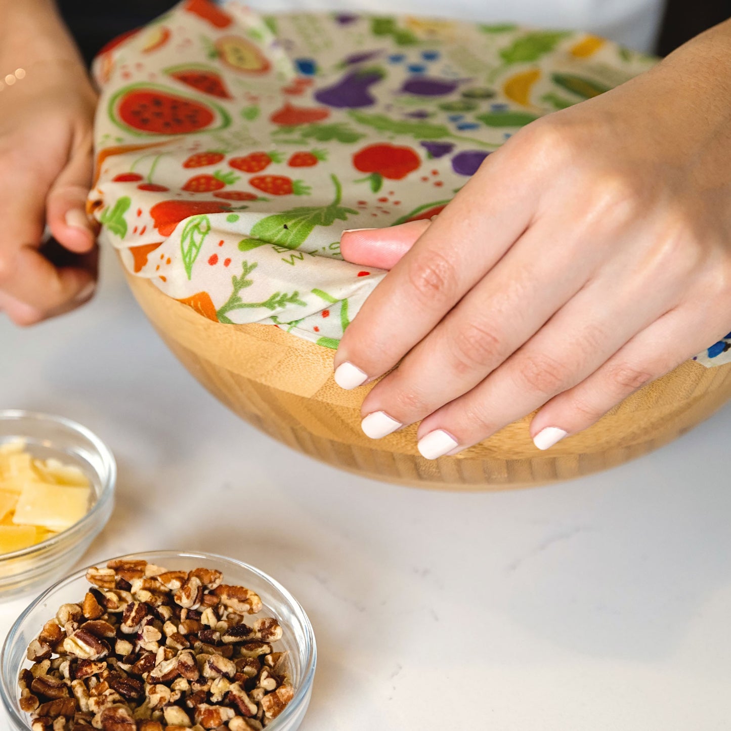 Person using a reusable food wrap on a wooden bowl with ingredients nearby.
