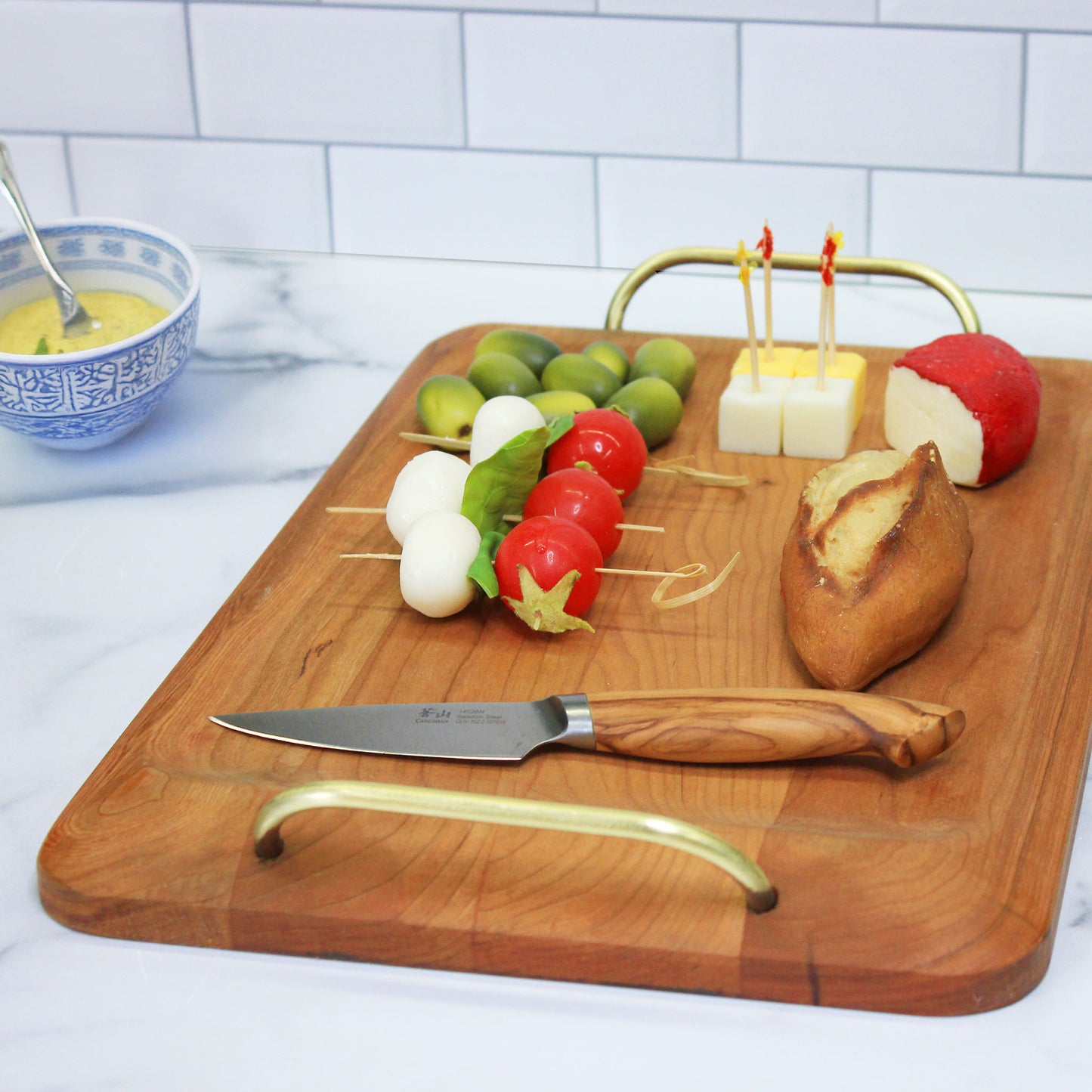JK Adams Cherry Handled Serving Board with Brass Handles, cheese, bread and olives on board.