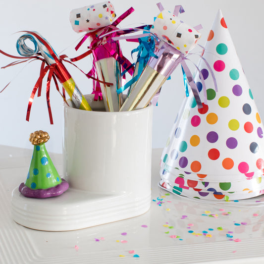 Colorful party hats and noisemakers on a white surface with confetti.