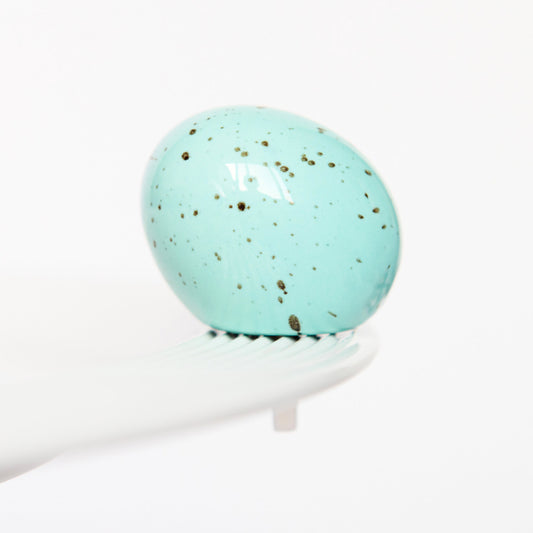 Turquoise marble egg, Nora Fleming mini, on a white platter with a white background