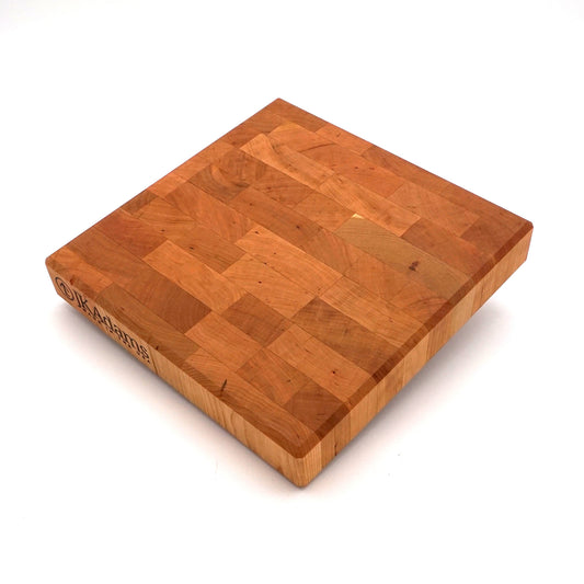 A square wooden butcher block cutting board with a warm honey-brown finish and visible end grain, photographed on a clean white background.