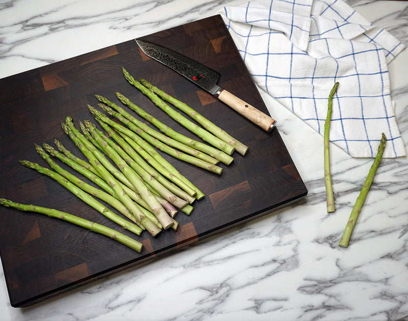 Green asparagus on a Walnut End Grain cutting board with a knife, on a marble surface.