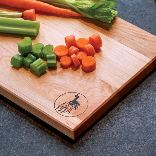 Wooden cutting board with chopped carrots and celery on a dark surface