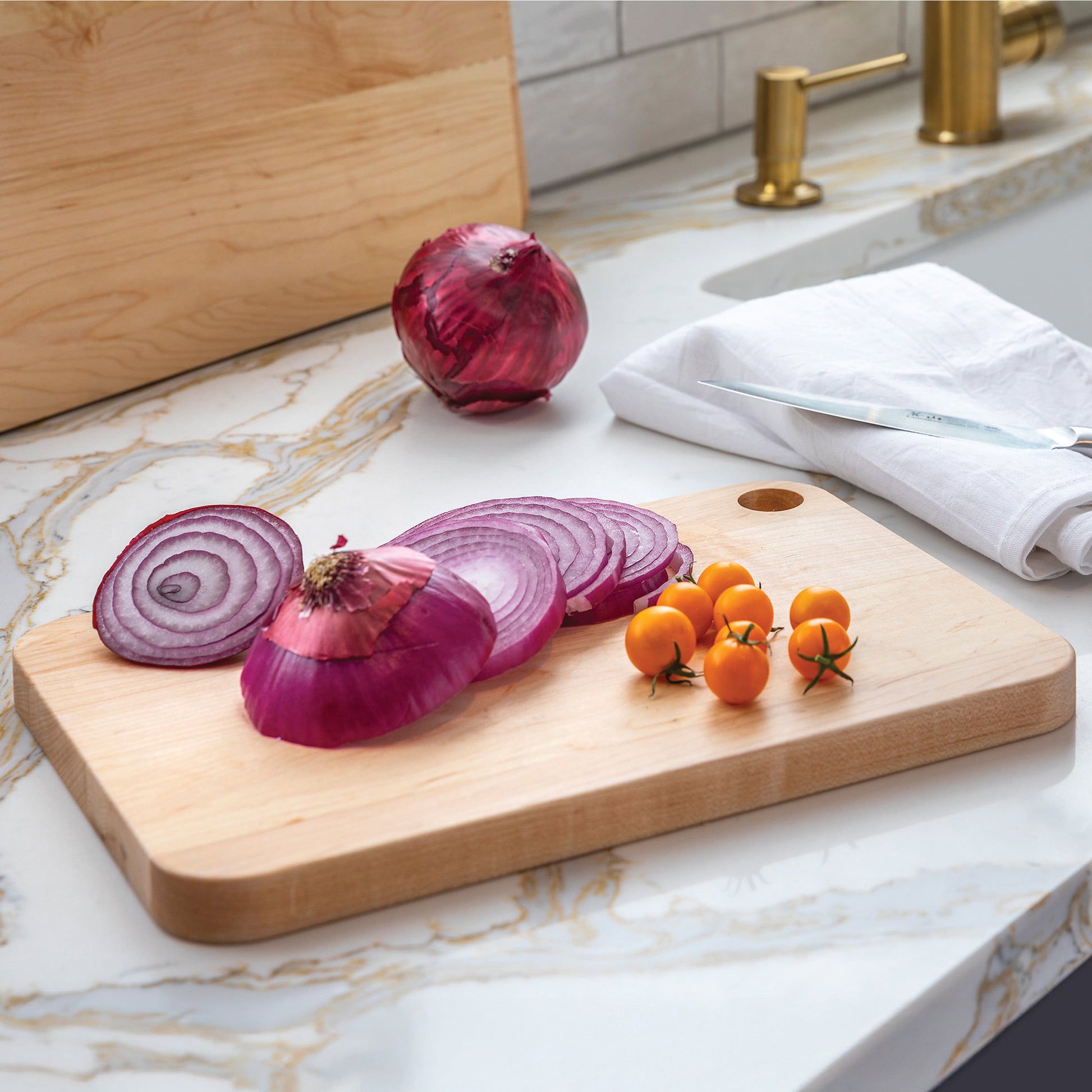 Sliced red onions and small tomatoes on a wooden cutting board with a marble countertop background.