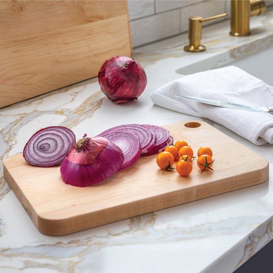 Sliced red onions and small tomatoes on a wooden cutting board with a marble countertop background.