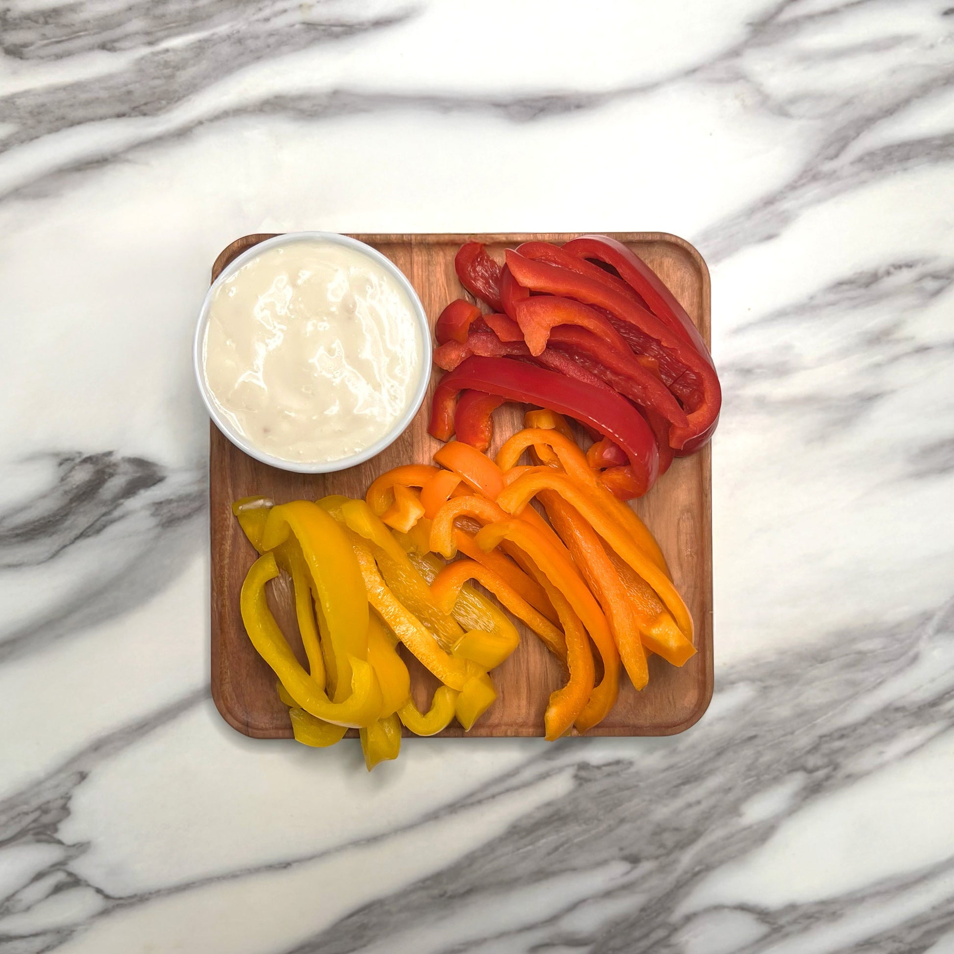 Cherry square wooden plate with a trio of bell pepper slices and a cup of ranch.
