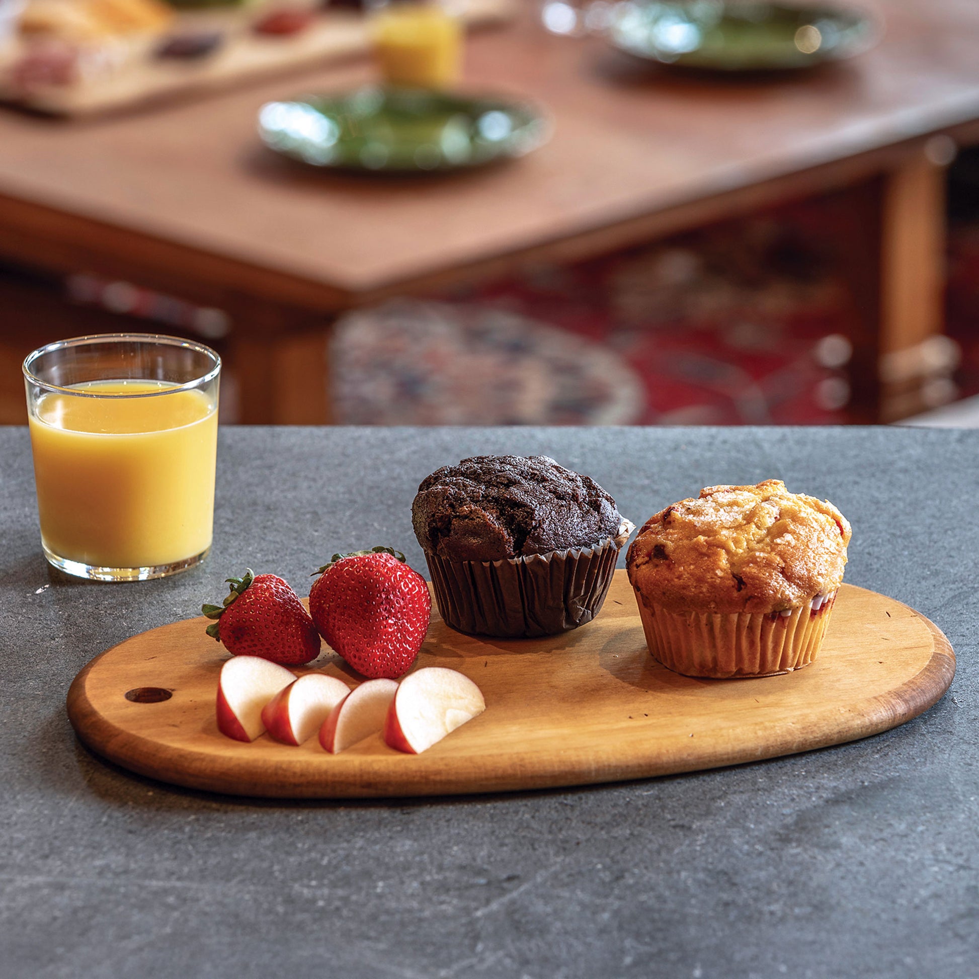 JK Adams Maple Artisan Oval Serving Board with muffins, apple slices, strawberries and a glass of orange juice.
