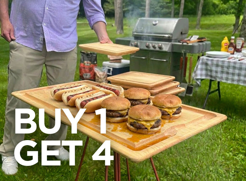 Person standing next to a table with burgers and hot dogs outdoors, with a grill and condiments in the background.