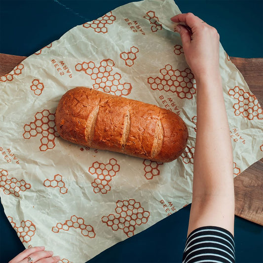 Loaf of bread on beeswax wrap with a hand holding the paper