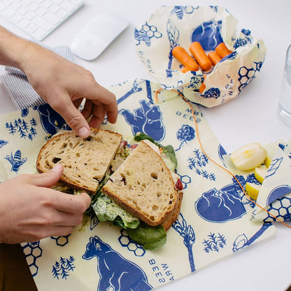 Person holding a sandwich on a patterned tablecloth with carrots and other snacks.