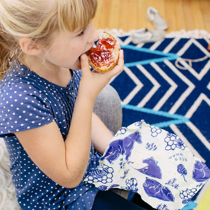 Child eating a pastry with jelly, sitting on a blue and white patterned rug.