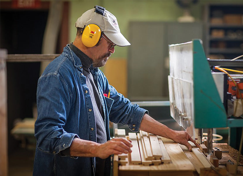 Man wearing hearing protection drilling wooden slats.
