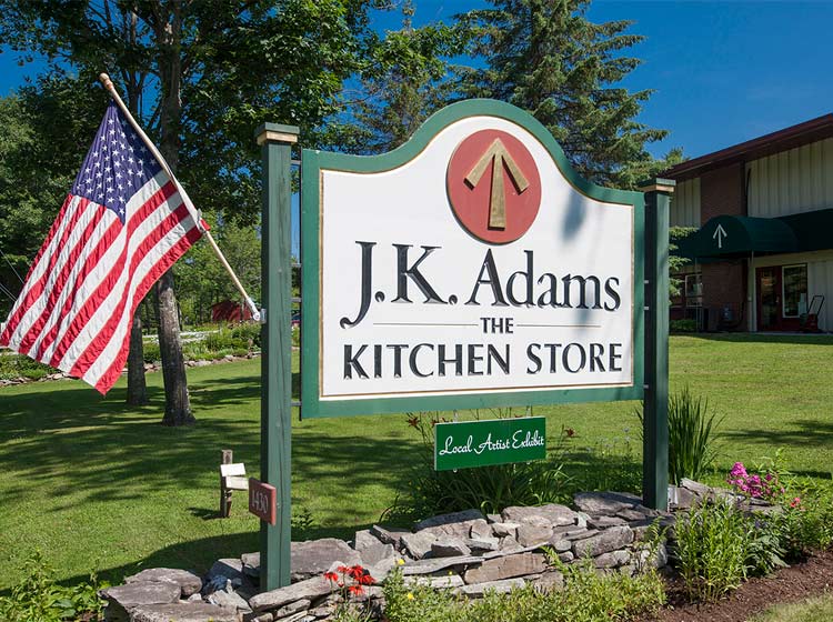 JK Adams sign in front of factory with American Flag.
