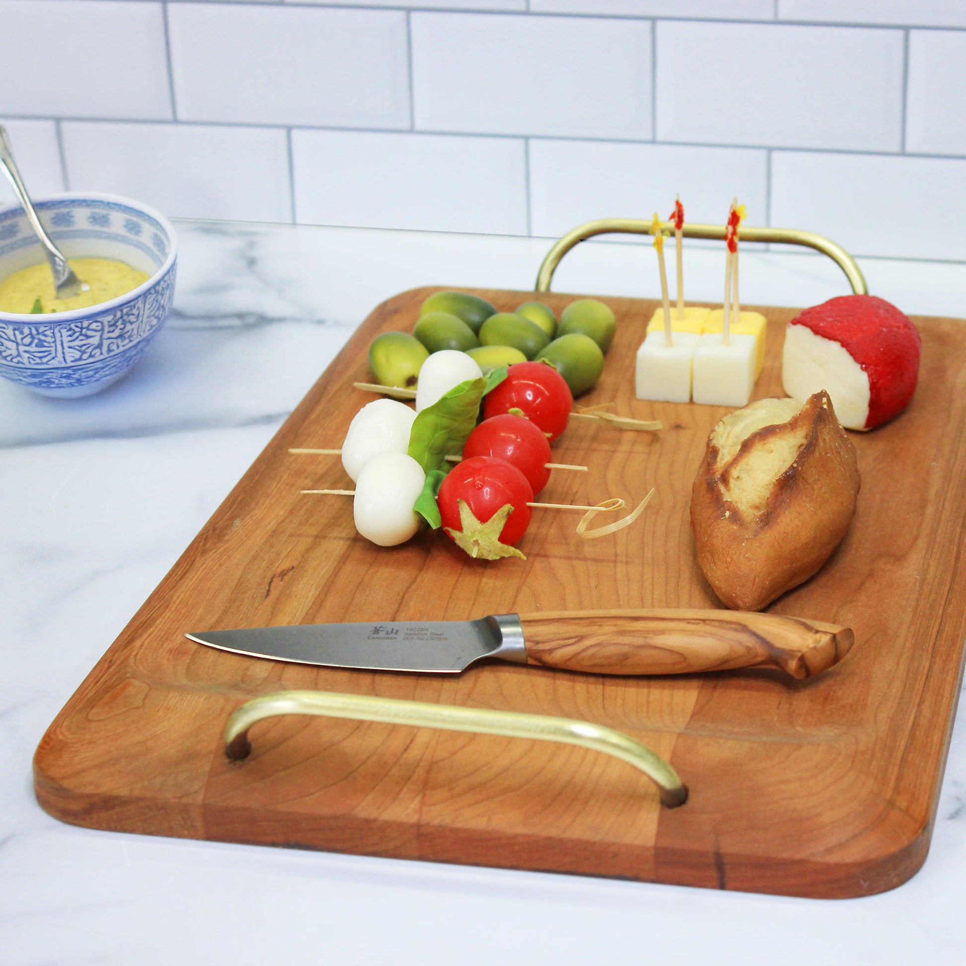 JK Adams Cherry Handled Serving Board with Brass Handles,  cheese, bread and olives on board.