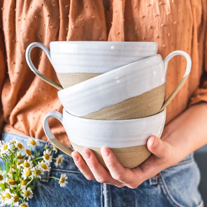 Stack of ceramic mugs with brown accents held by a person against an orange textured background