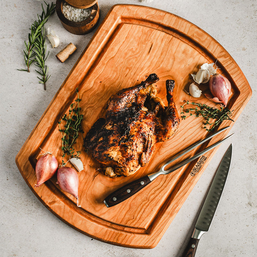 A cherry carving board with a roast chicken, shallots and a carving set.
