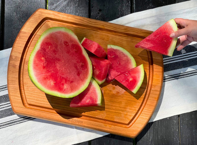Cherry carving board with watermelon slices and a person grabbing a slice.

