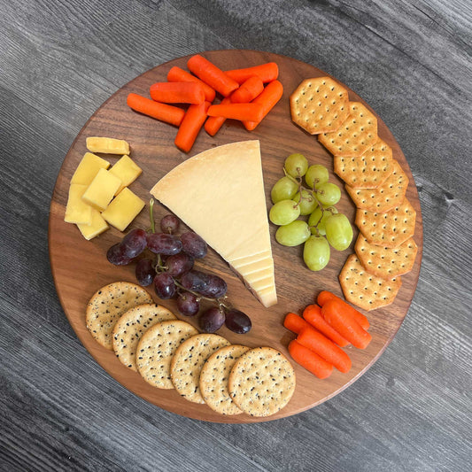 Walnut Lazy Susan with assorted snacks including cheese, crackers, and vegetables on a gray surface.