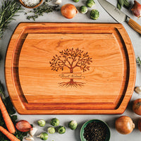Wooden cutting board with tree design and engraved text, surrounded by vegetables on a light surface.