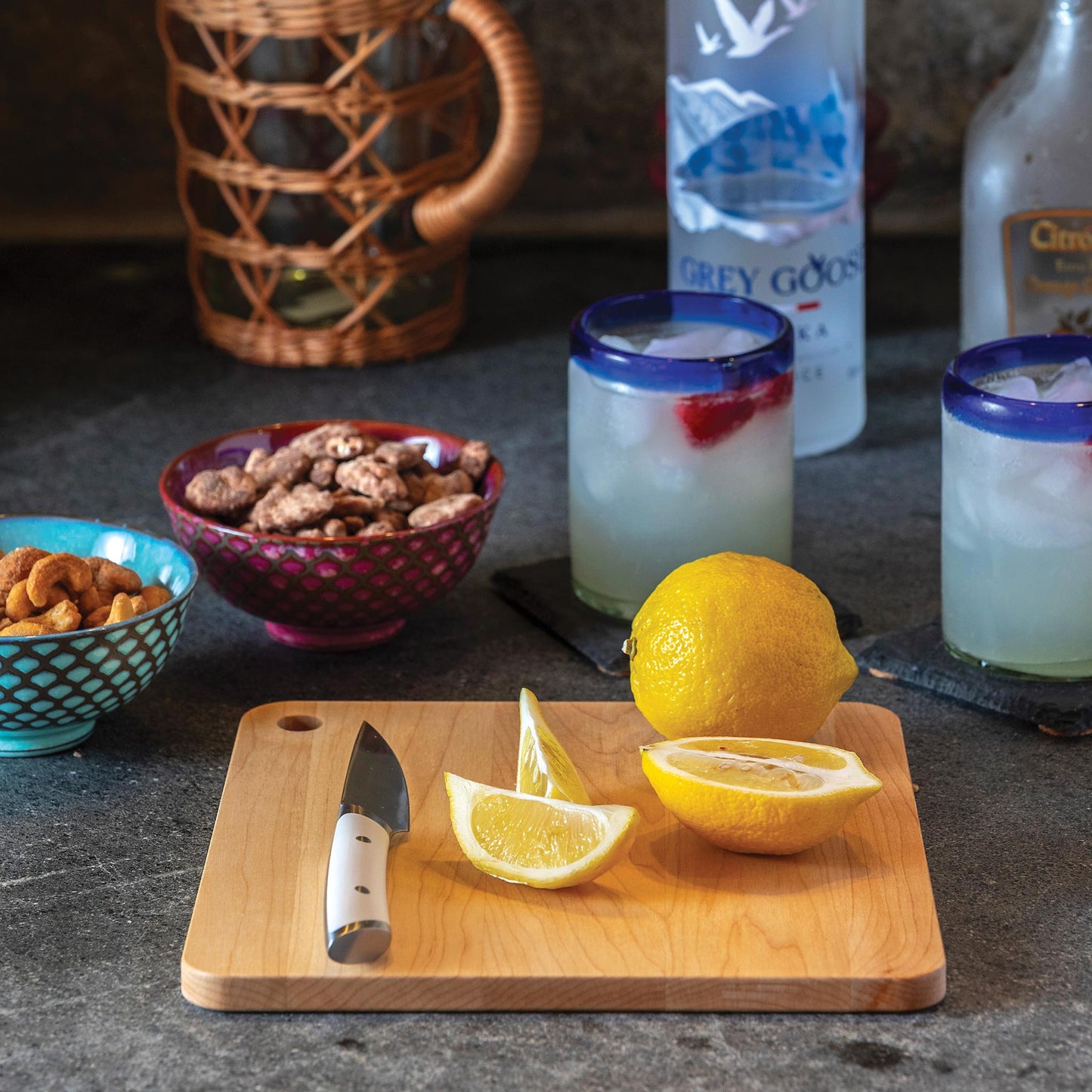 Lemons on a cutting board with drinks and snacks in the background