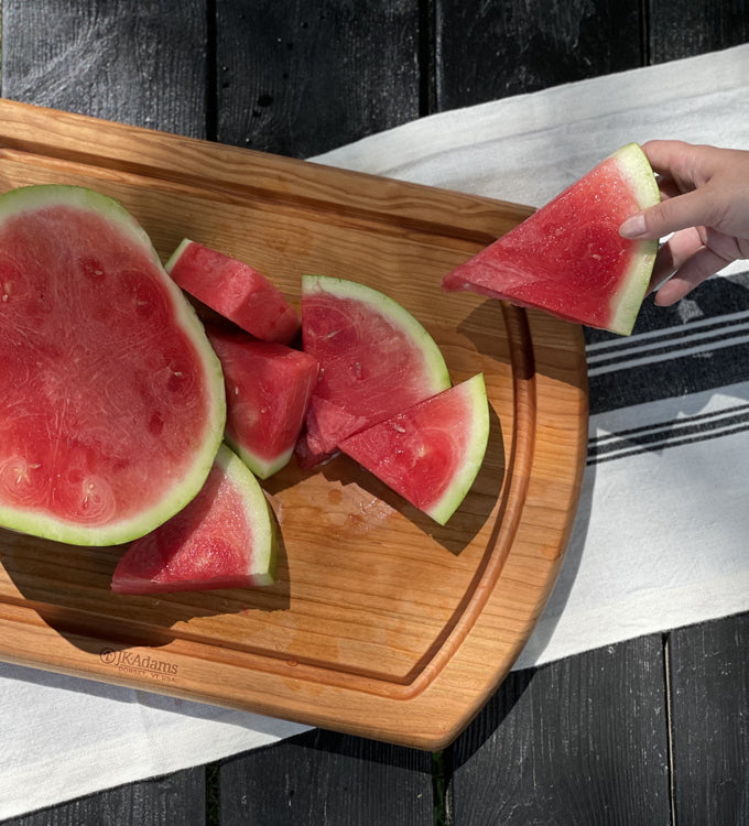 Cherry carving board with watermelon slices and a person grabbing a slice.
