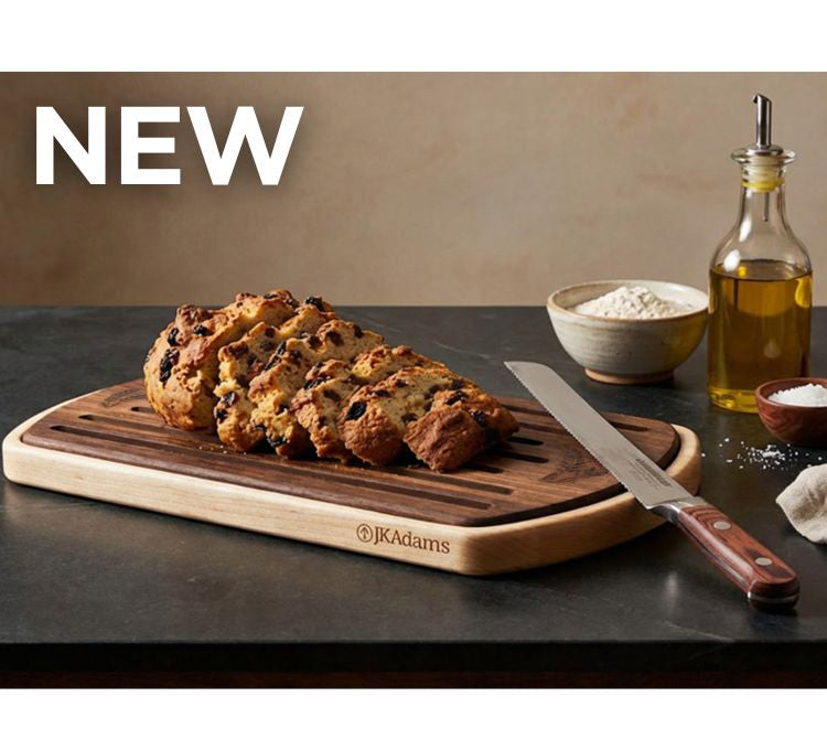 Loaf of bread on a wooden cutting board with a knife, oil bottle, and flour bowl in the background.
