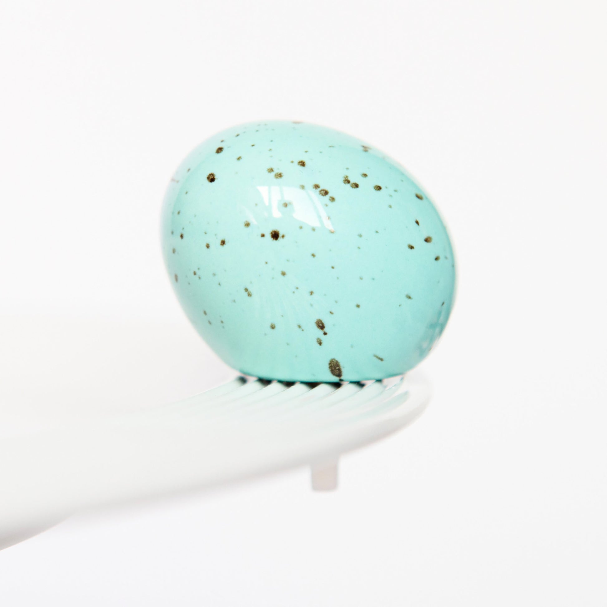 Turquoise marble egg, Nora Fleming mini, on a white platter with a white background
