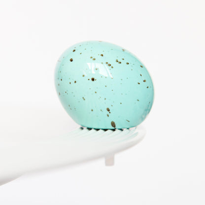 Turquoise marble egg, Nora Fleming mini, on a white platter with a white background