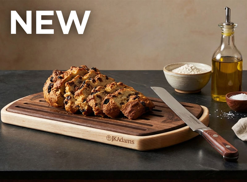 Loaf of bread on a wooden cutting board with a knife, oil bottle, and flour bowl in the background.