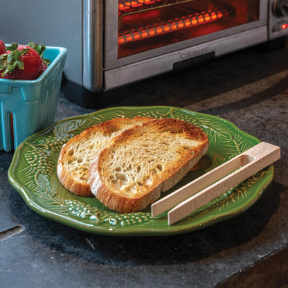 Two slices of toast on a green plate with wooden tongs, toaster oven in the background
