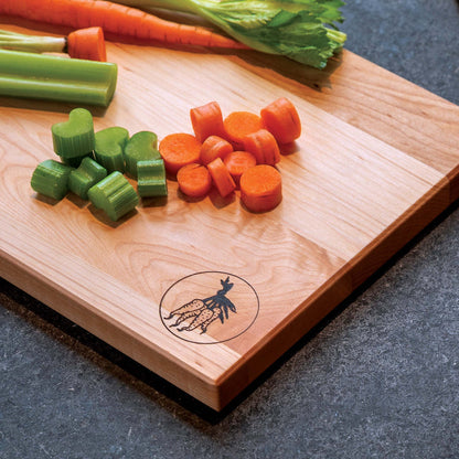 Wooden cutting board with chopped carrots and celery on a dark surface