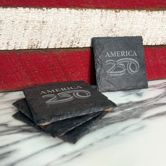 Slate coasters with 'AMERICA 250' design on a marble surface with a wooden background.