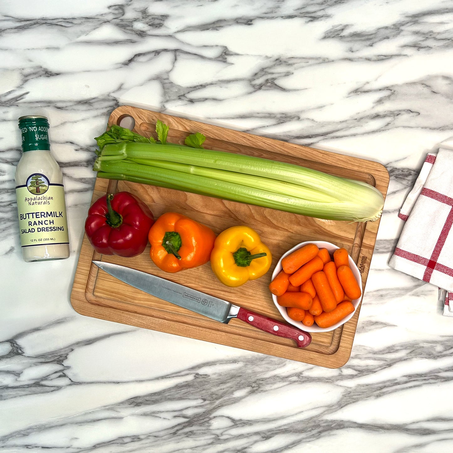 Wooden cutting board with vegetables and a bottle of buttermilk ranch dressing on a marble countertop.